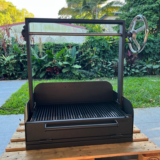Portable grill on a wooden pallet outdoors with greenery in the background