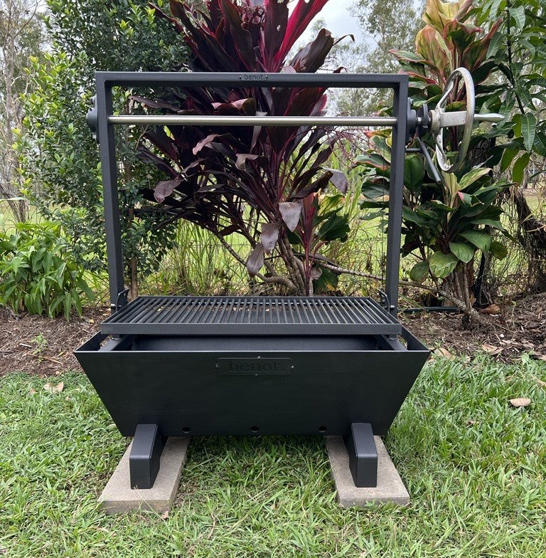 Black outdoor fire pit grill on grass with plants in the background
