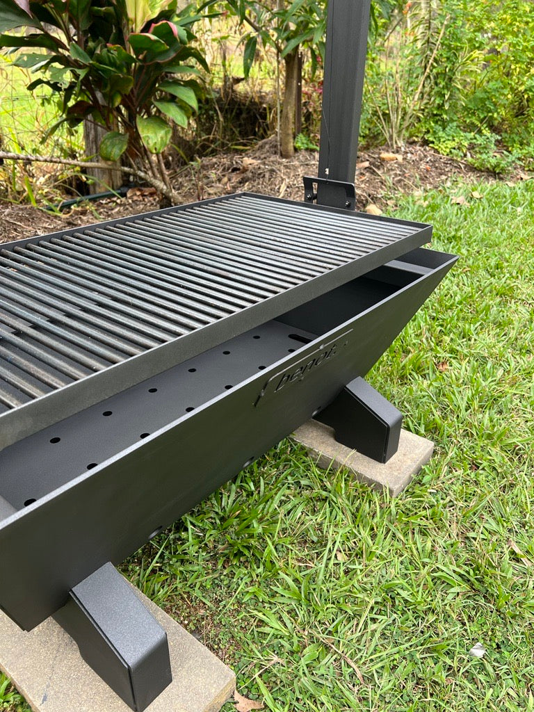Black fire pit bbq grill on a concrete block outdoors with greenery in the background
