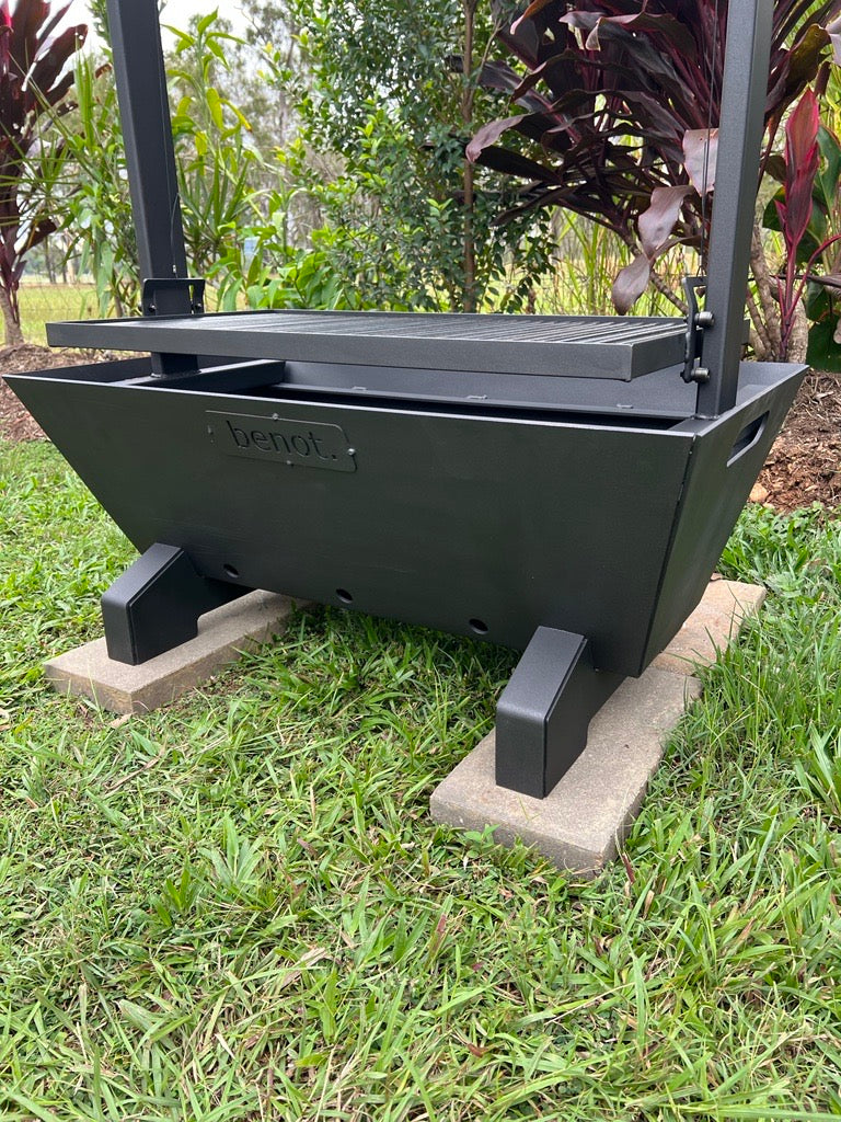 Black metal fire pit BBQ santa maria parrilla asado grill on a grassy area with plants in the background