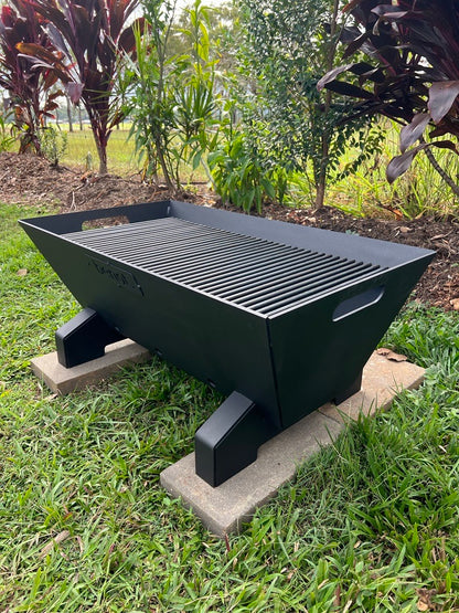 Black outdoor Fire pit bbq grill on a grassy area with plants in the background