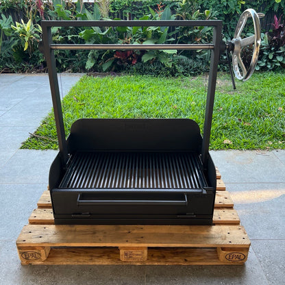 Black outdoor parrilla grill on a wooden pallet with a garden background